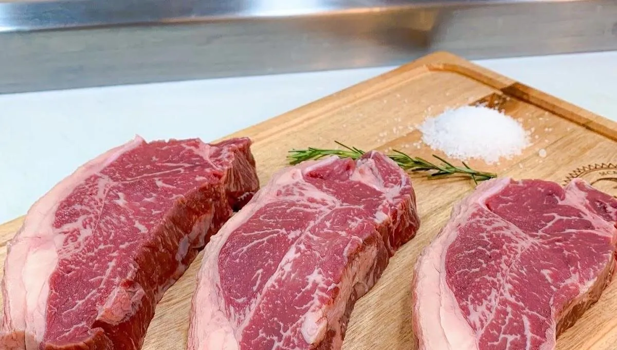Três bifes crus marmorizados sobre tábua de madeira com alecrim e sal grosso